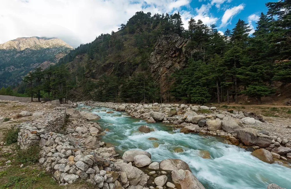 Fast-flowing turquoise river rushing over rocks in Harsil, flanked by pine forest and steep mountains