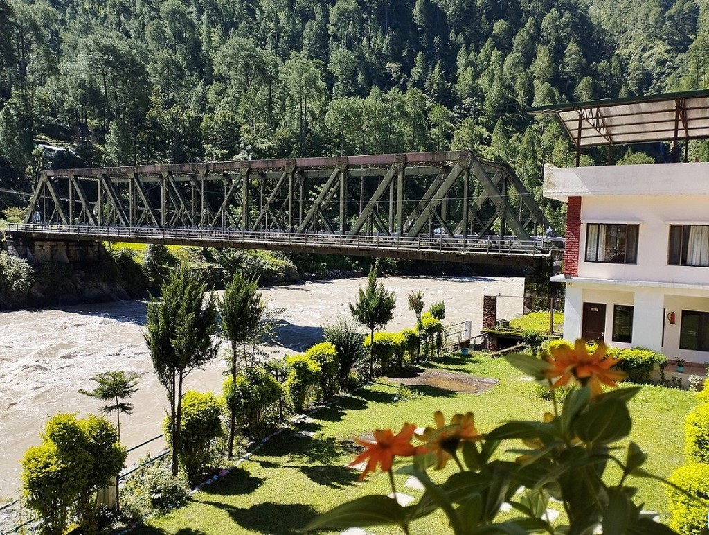 Shiv Parivar Resort gardens, river, metal bridge, and forested Himalayan slope in Uttarkashi